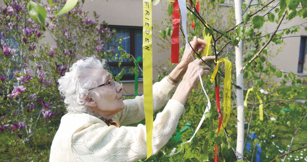Frau knüpft Bänder mit Wünschen an einen Maibaum