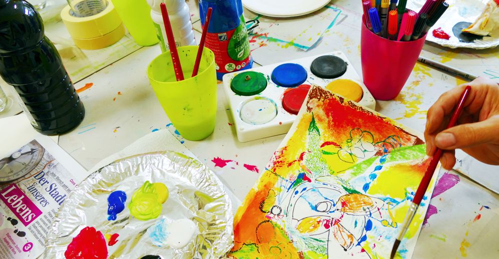 Tisch mit Farbtöpfen, Pinseln, Zeichenpapier und anderen Kreativ-Utensilien