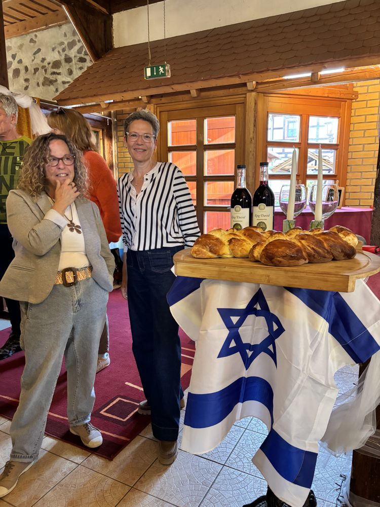 Zwei Frauen stehen neben einem Tisch mit Brot und Wein bei einer Schabbat-Feier