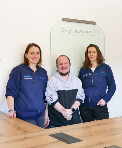 Praktikant WaldWerkStatt+ steht mit zwei Mitarbeiterinnen am Küchentisch