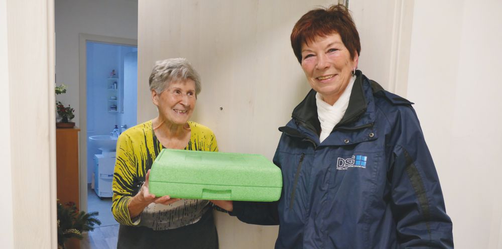 Fahrerin von Essen auf Rädern übergibt Menüschale an Seniorin