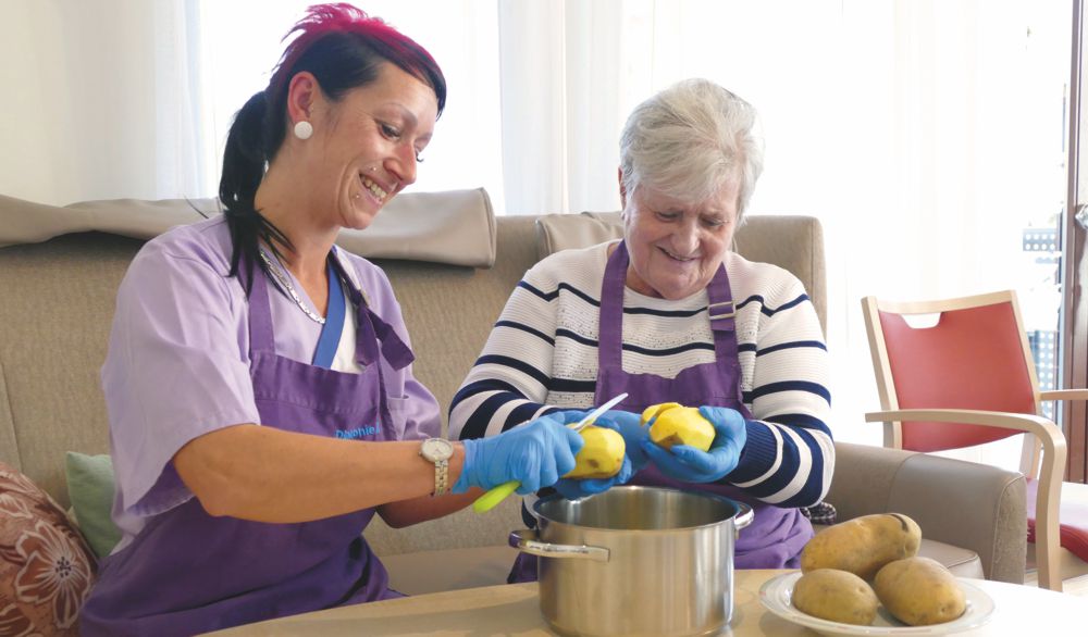 Pflegerin und Heimbewohnerin schälen Kartoffeln