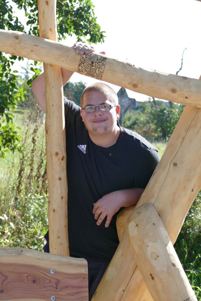 Jugendlicher schaut lächeldn durch Holzskulptur