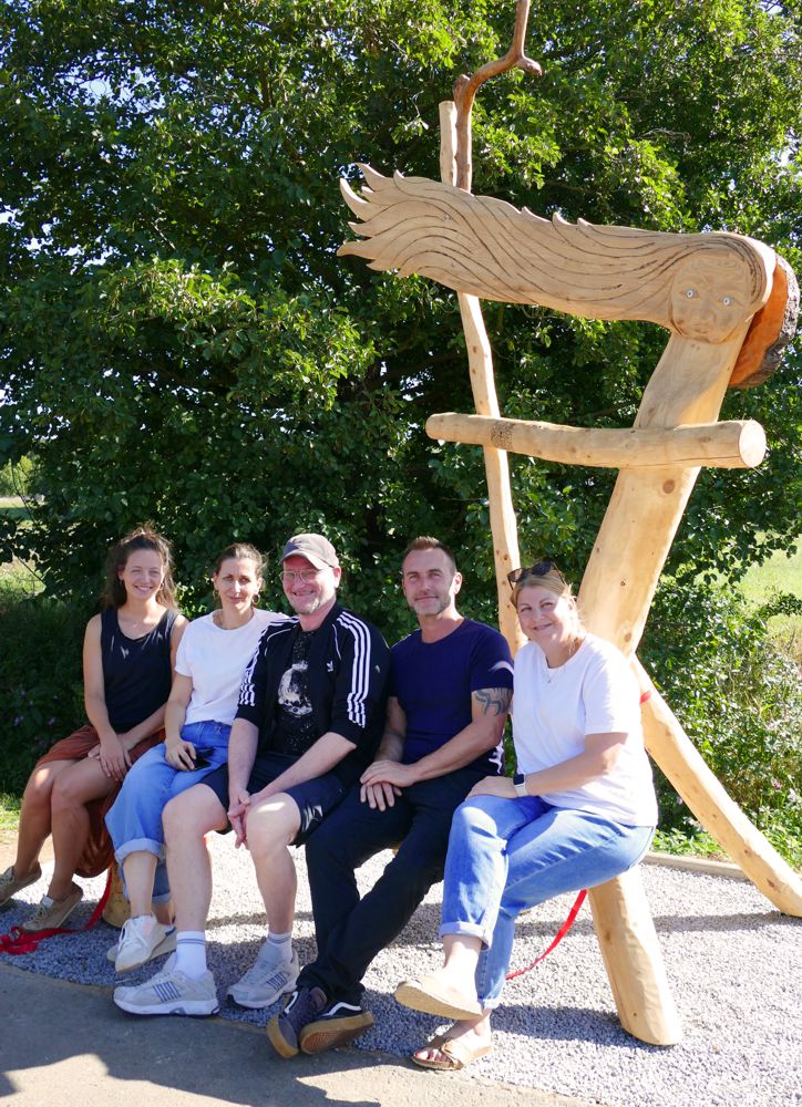 Team der WaldWerkStatt+ sitzt auf Bank der neuen Holzsskulptur