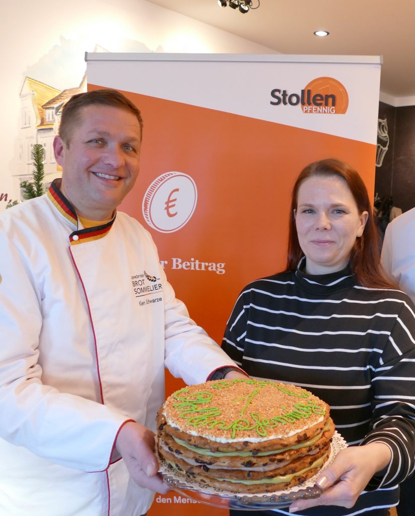 Bäcker übergibt an Sozialarbeiterin großen essbaren "Stollenpfennig"