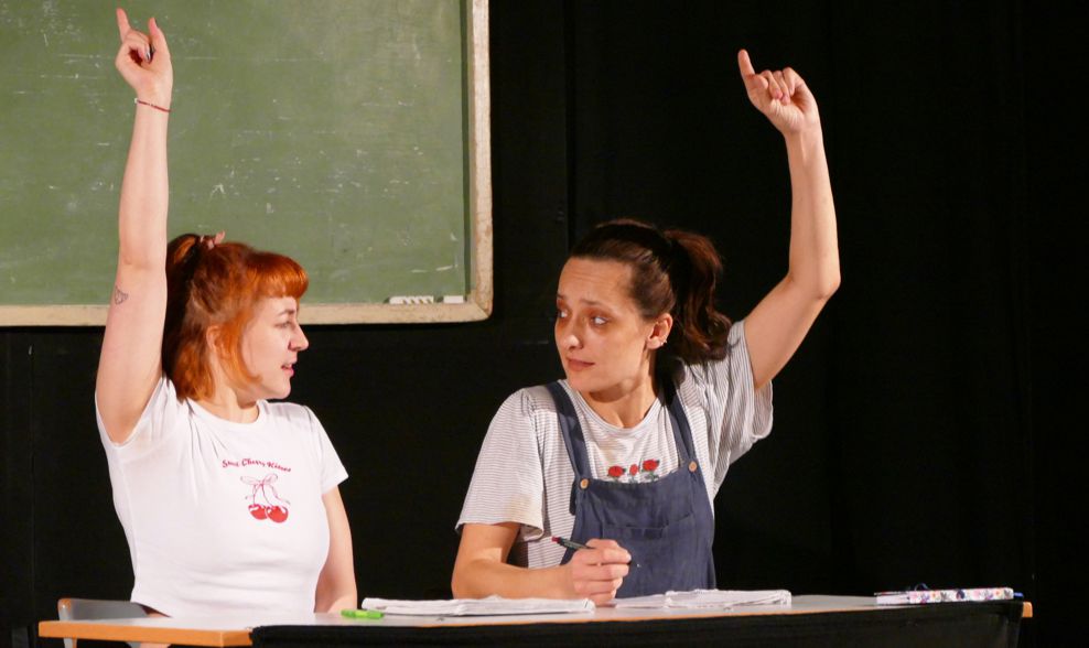 2 Schauspielerinnen sitzen vor Schultafel und melden sich bei der Aufführung eines Stücks über Mobbing im Kino Groitzsch